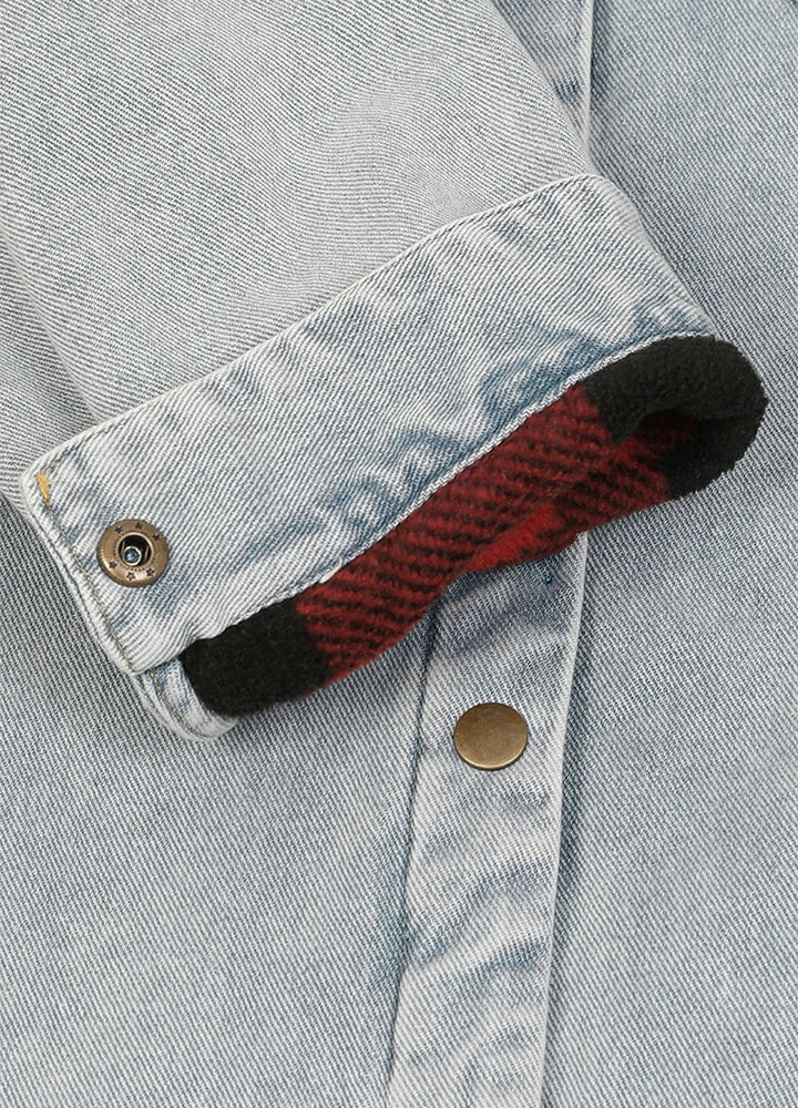 Close-up of a light blue denim jacket or shirt cuff turned up, showing a red and black plaid lining with a metal snap button.