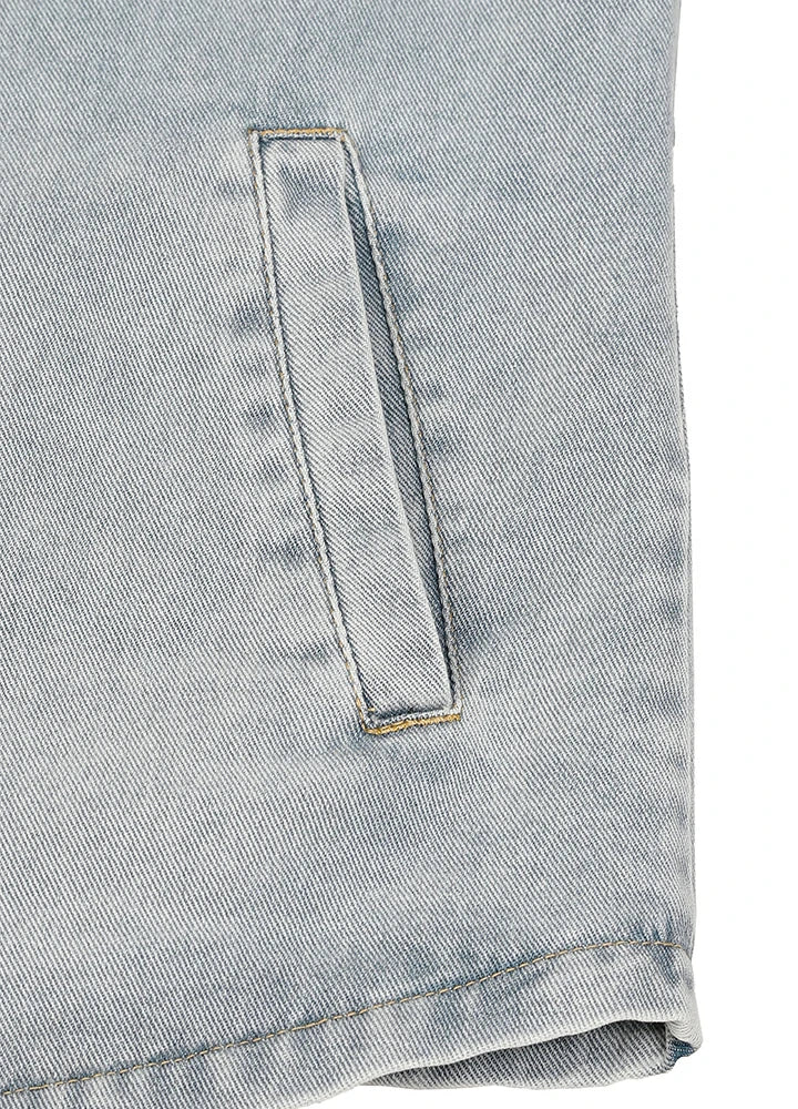 Close-up of a light blue denim fabric with a vertical welt pocket and visible stitching.