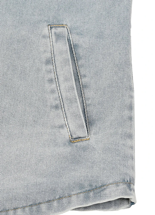 Close-up of a light blue denim fabric with a vertical welt pocket and visible stitching.