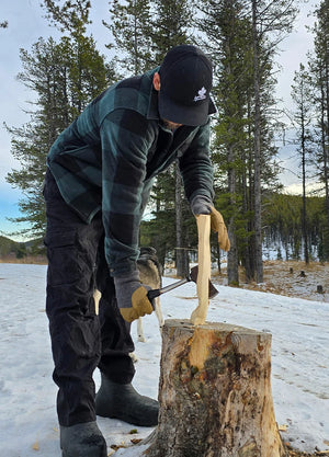 Front view of a man in a black green men's cozy plaid sherpa lined shirt jacket is chopping wood