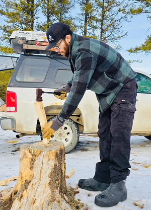 Side view of a man in a black green men's cozy plaid sherpa lined shirt jacket, chopping wood