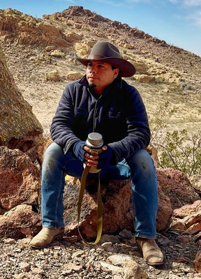 Front view of a man in a twill grey men's warm sherpa lined fleece shirt jacket sitting on a rock