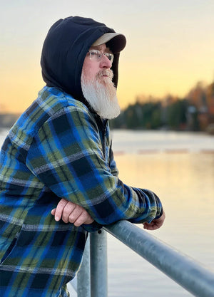 Side view of a man wearing green blue men's sherpa lined flannel jacket leaning on a railing