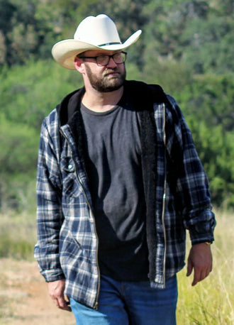 Front view of a man in a navy khaki men's plaid flannel hooded jacket walking in the grass   