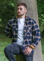 Front view of a man wearing a navy blue coffee men's durable flannel cotton shirt leaning against a tree