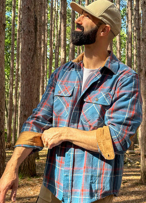 Side view of a man wearing a blue plaid flannel shirt for men adjusting the cuffs
