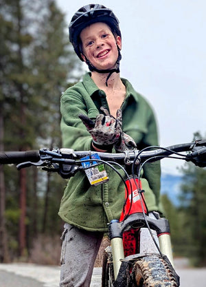 A boy wearing an army green plaid fleece button-down shirt jacket rides a mountain bike.
