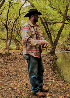 Side view of a man wearing a black and grey men's Aztec shirt jacket, standing sideways while fishing