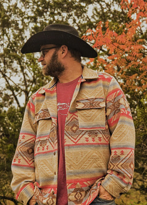 Front view of a man wearing a black and grey men's Aztec shirt jacket with his hands in the pockets, looking sideways