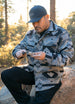 Man in a patterned Aztec jacket and cap outdoors, holding a knife.