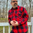A man leaning against a fence in a red buffalo plaid men's heavyweight flannel plaid shirt