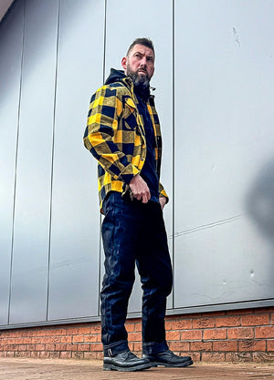 Side view of a man in a black and yellow 10.6 oz flannel plaid shirt for men standing in front of a wall
