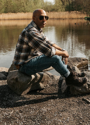 Side view of a man in a coffee white men's stalwart heavyweight cotton plaid sitting on a stone