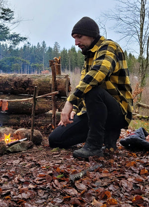 Side view of a man in a yellow black men's 10.6 oz flannel plaid shirt crouching by the fire