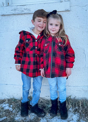 Children wearing red and black plaid flannel jackets snuggling on a cold winter day