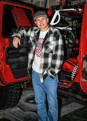 Front view of a man in a black white men's cozy snap button flannel shirt jacket leaning against a car door