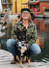 A woman in a forest green printed flannel plaid shirt with a dog